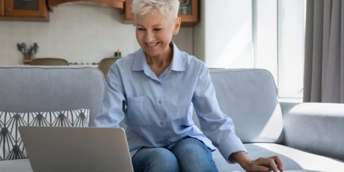 smiling mature woman grandma sit on sofa engaged in accounting paperwork calculate regular taxes bills sum make payments online on laptop happy elderly female use ebank application to pay utilities