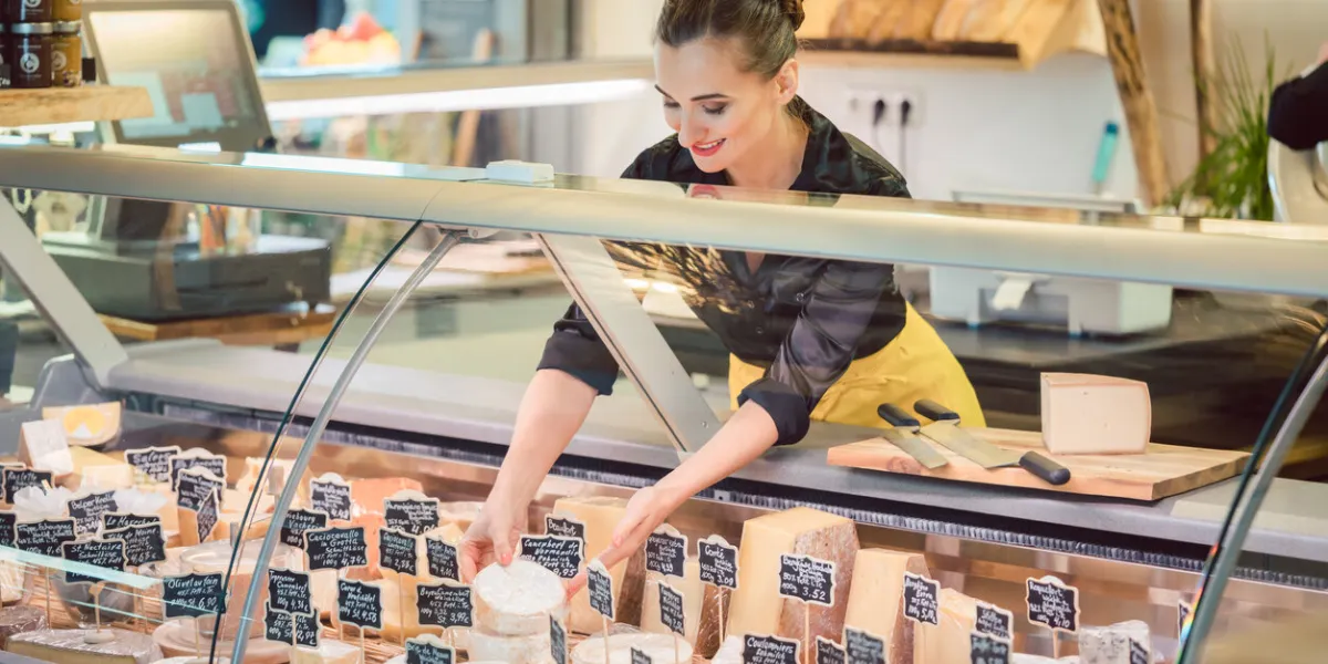 shop clerk woman sorting cheese in the supermarket display to sell it