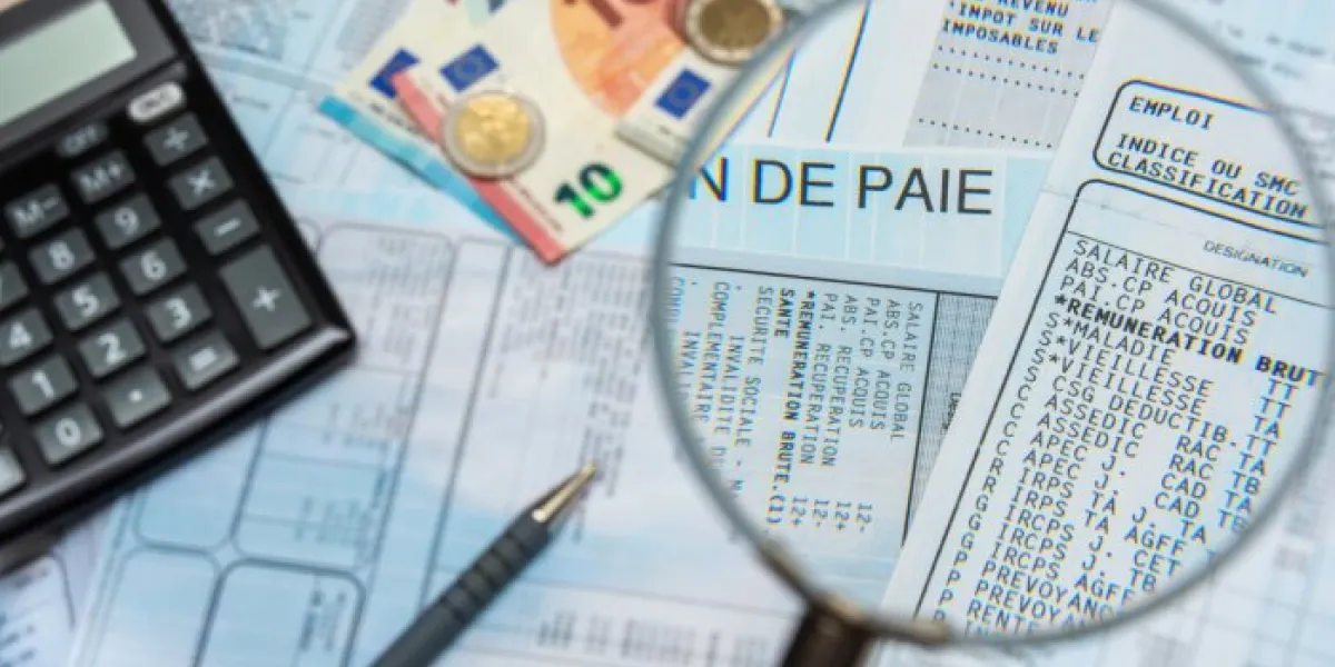 blurred french payroll with a calculator, a pen, euro cash, and a magnifying glass sharp focus only through the magnifying glass