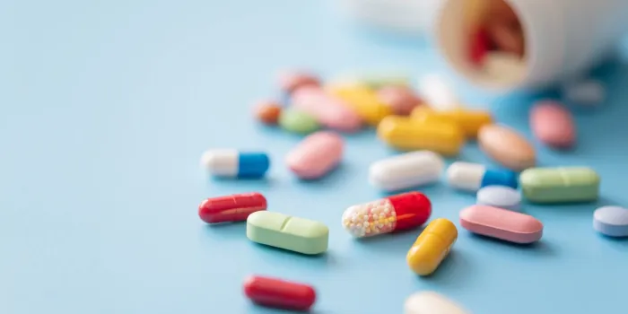 colorful pills scattered from white plastic pill bottle on blue background shallow dof