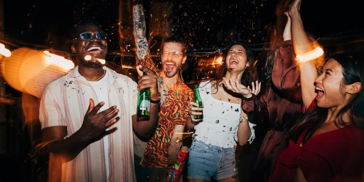 a cheerful group of multiracial friends is celebrating and having fun with confetti at the open-air summer rooftop nightclub they are having a blast, dancing and drinking beer