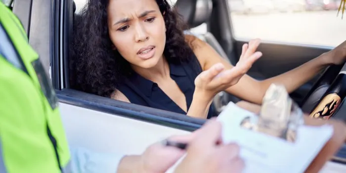shot of a young businesswoman looking upset at receiving a ticket from a traffic officer