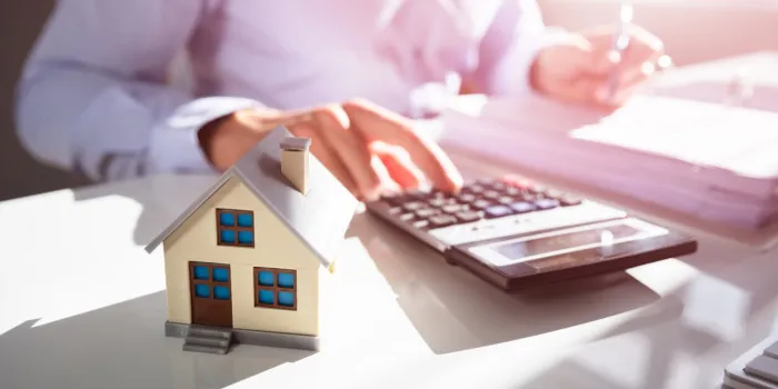 close-up of a person hand doing property tax calculation with house model on the table
