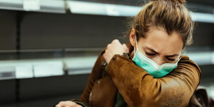sick woman buying in supermarket and coughing into elbow during covid-19 pandemic