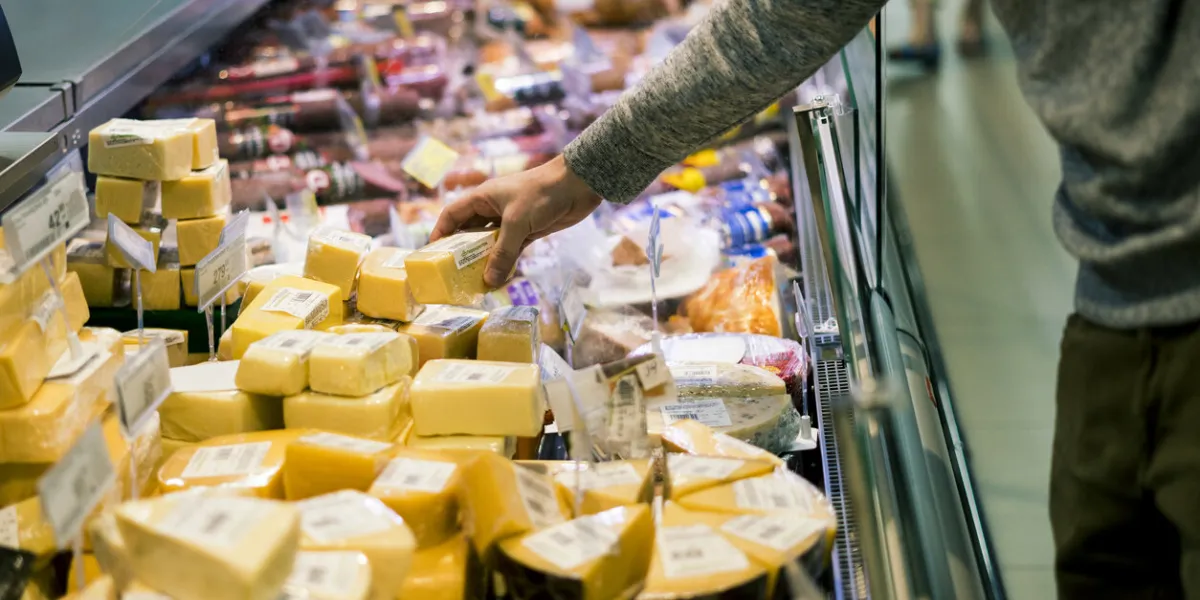 close up person choosing piece of cheese in food shop
