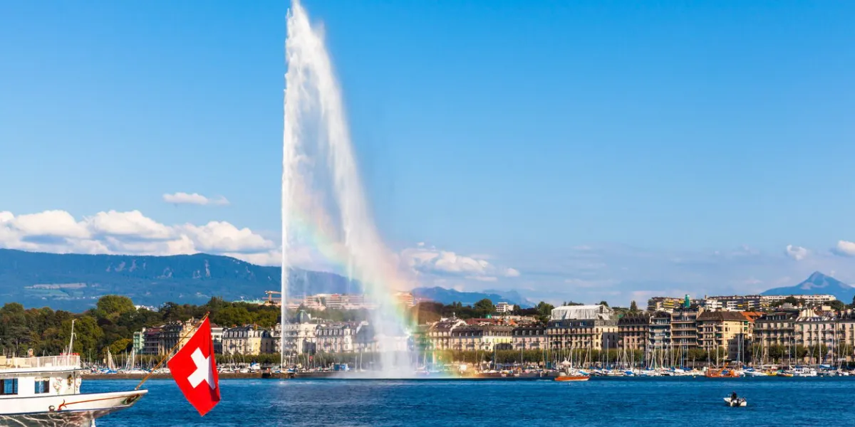 beautiful view of the water jet fountain with rainbow in the lake of geneva and the cityscape of geneva at sunset, switzerland