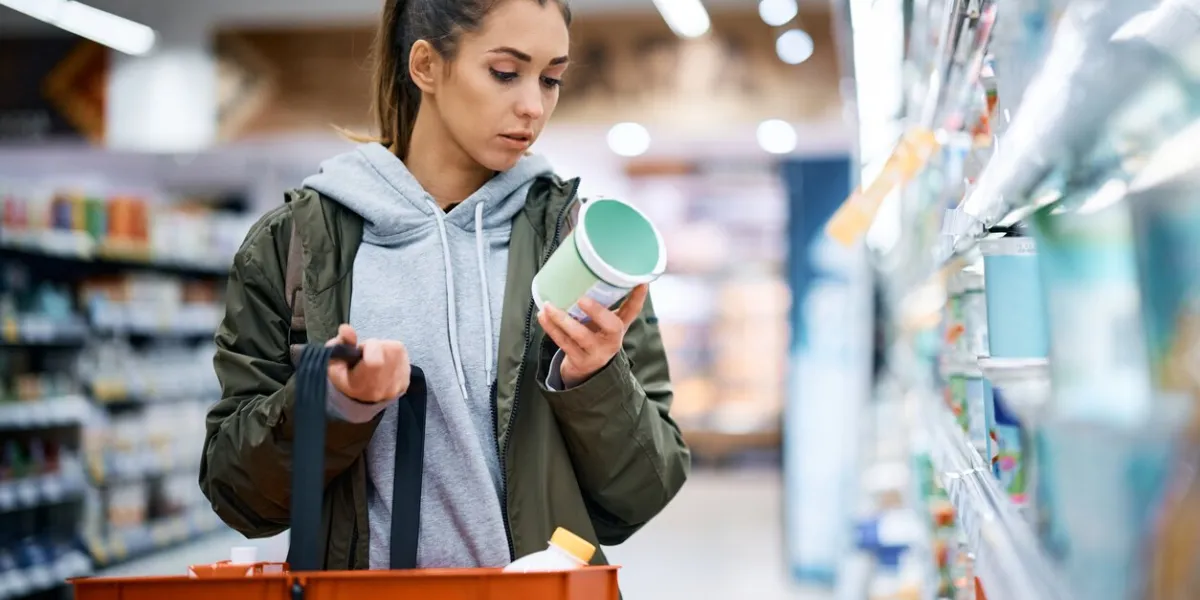 young woman reading nutrition label while buying diary product in supermarket