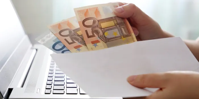 woman pulls money out of an envelope on laptop background, wages, bonus or bribe concept