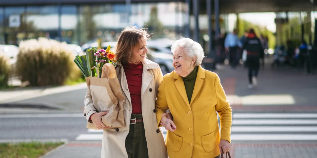 mature granddaughter carrying groceries out to her grandmother's car senior woman shopping at the shopping center, needing help loading groceries into the car