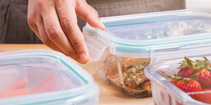 a woman meal preps in the kitchen she is putting black berries, strawberries, peas, and nuts into clear glass food storage containers with lids