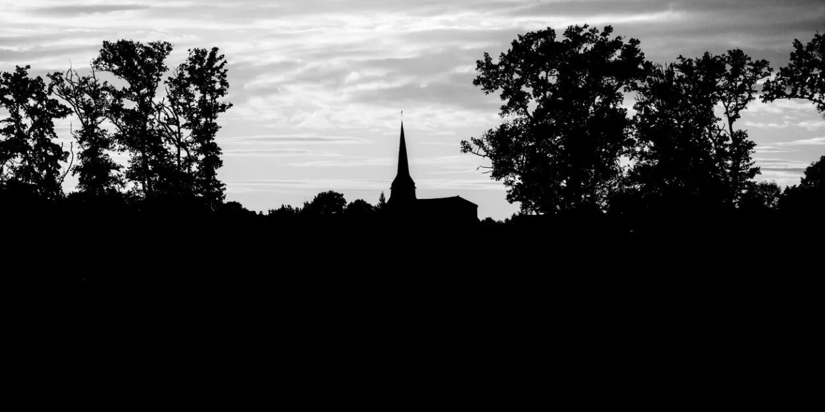 landscape of saint-gence where you can see the church in the center, surrounding trees, on a sunset in black and white