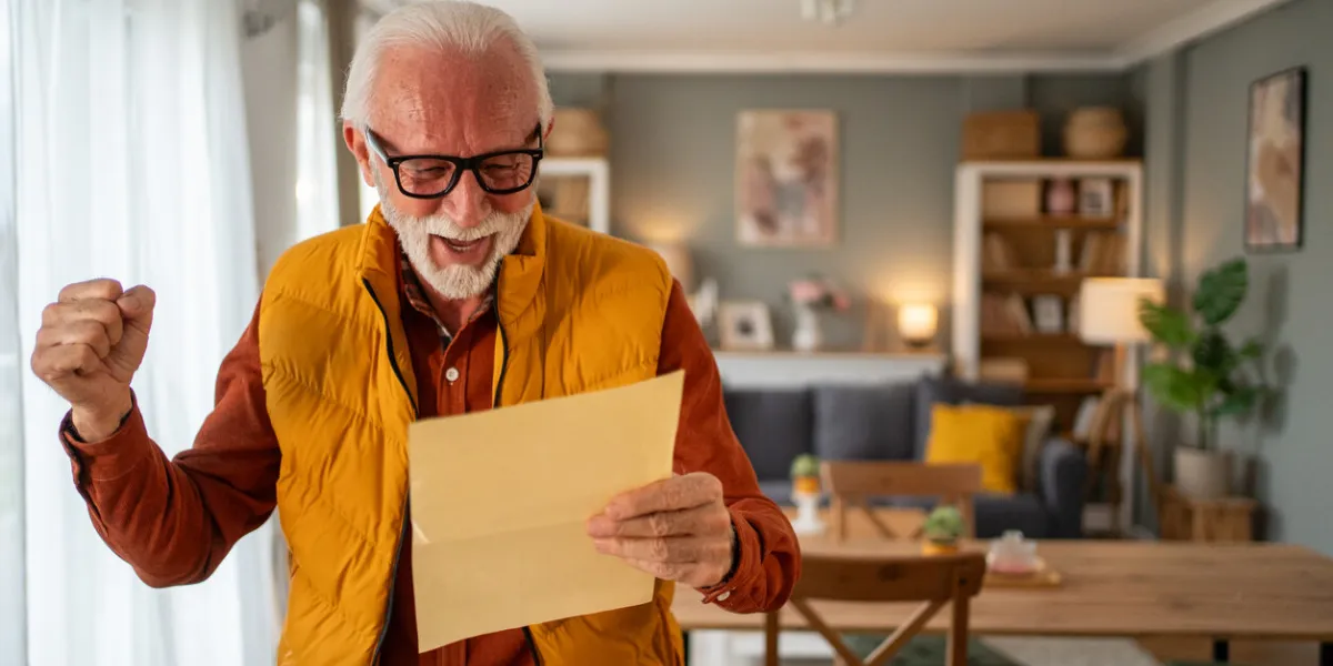 excited retired man reading a letter filled with good news, celebrating with a raised fist while sitting in a modern, cozy living room, radiating joy and contentment