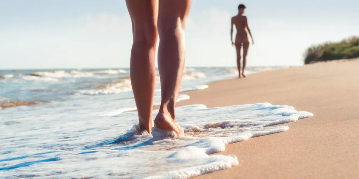 nude young girls walk on the beach in the waves of the surf on a summer day