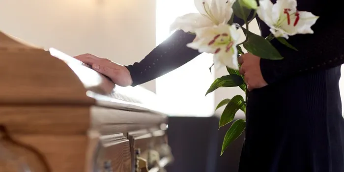 people and mourning concept - woman with white lily flowers and coffin at funeral in church