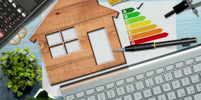 energy efficiency rating graph on a desk with a wooden house model, calculator, folding ruler, drawing compass, pencil and a computer keyboard