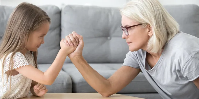 serious old grandma and little granddaughter arm wrestling, grandchild girl and grandmother competing playing together, grandparents and children generations confrontation, family conflicts concept