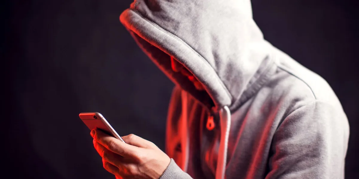 man wearing hoody sweater with mobile phone in hands crime and hacking concept