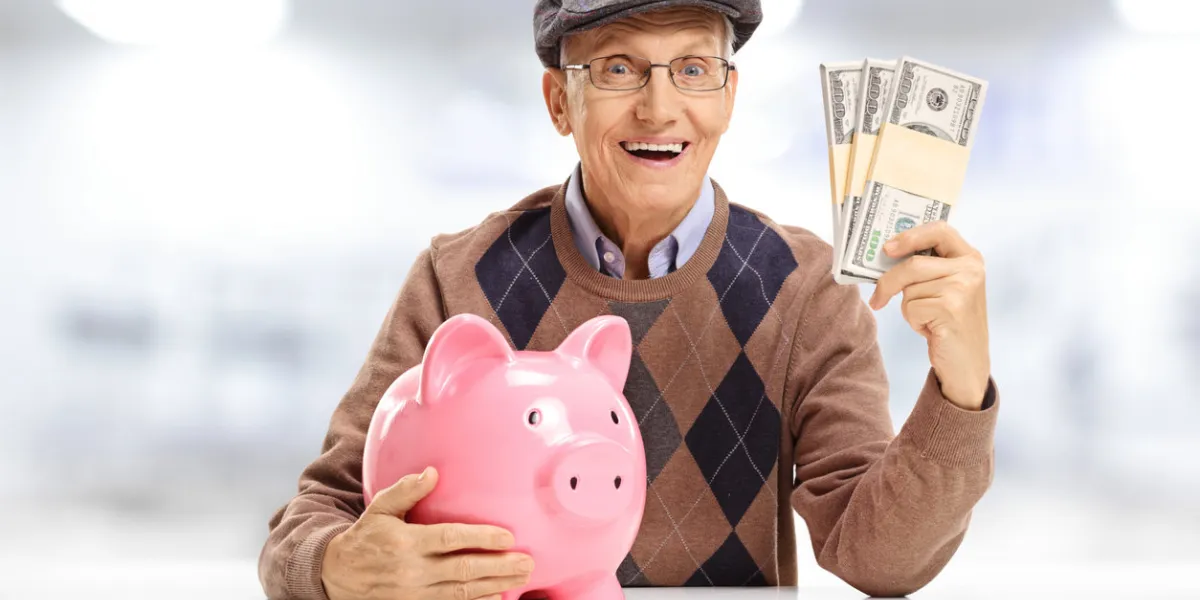 senior with a piggybank and bundles of money seated at a table