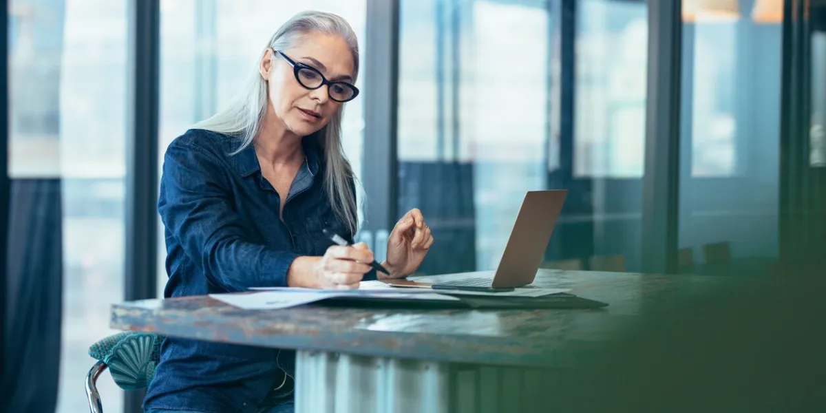 portrait of senior woman sitting at table in office and reading few paper work business manager working on some documents at office