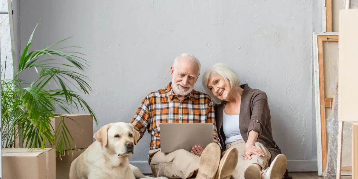 happy senior couple using laptop sitting on floor and husband petting dog lying near