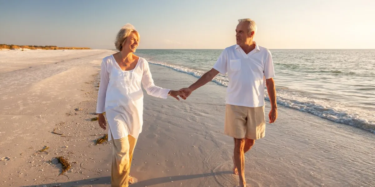 happy senior man and woman old retired couple walking and holding hands on a beach at sunset