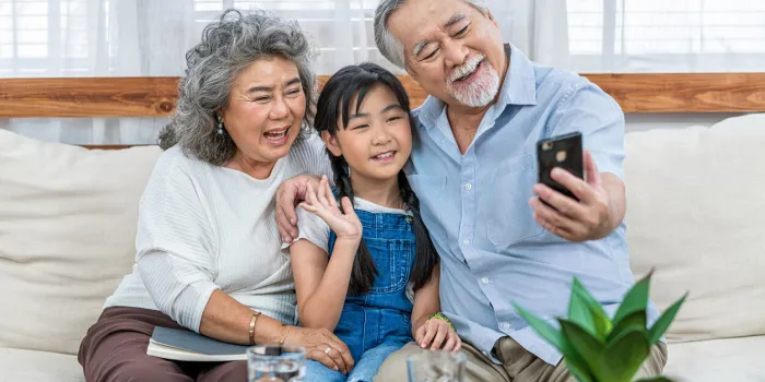 asian couple grandparent taking selfie with granddaughter with happy feeling by mobile phone in house
