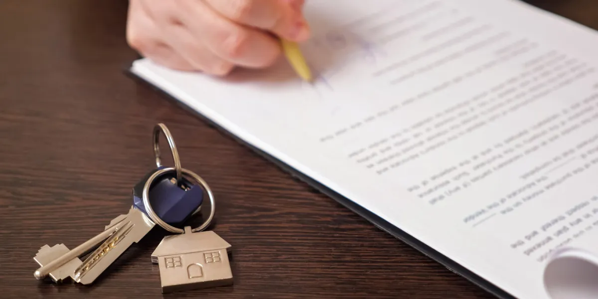 man client signs new apartment purchase contract with pen near keys with house shaped breloque put on table extreme close view