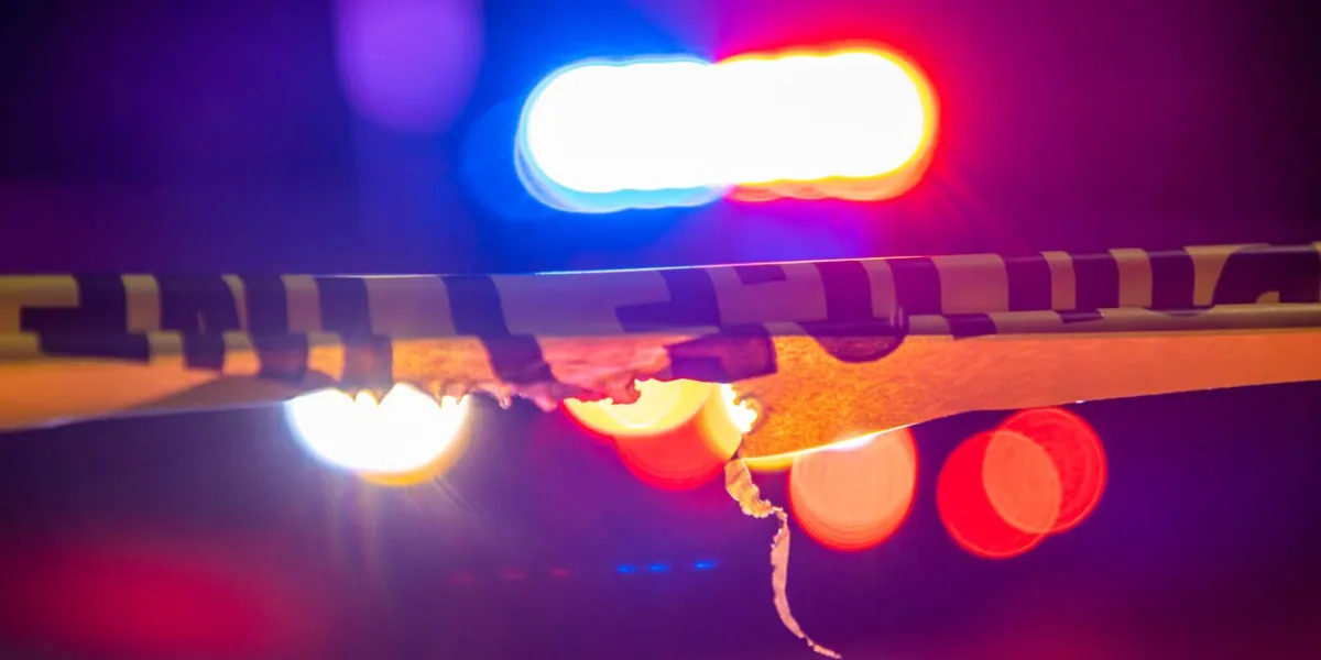 a defocused police car sits behind crime scene tape with flashing lights at night