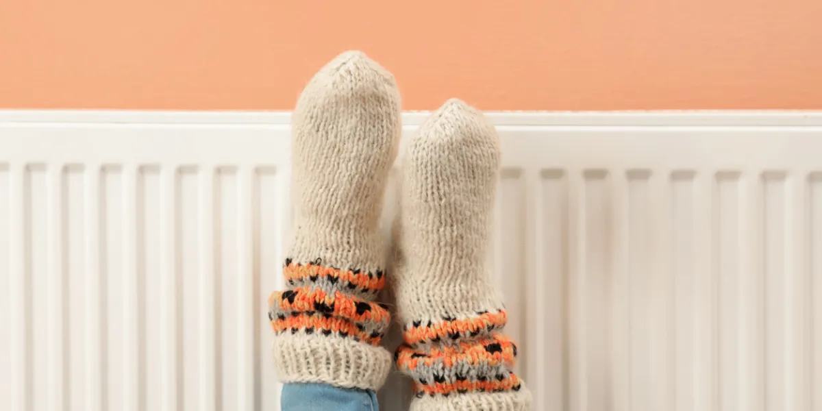 woman warming legs on heating radiator near color wall, closeup