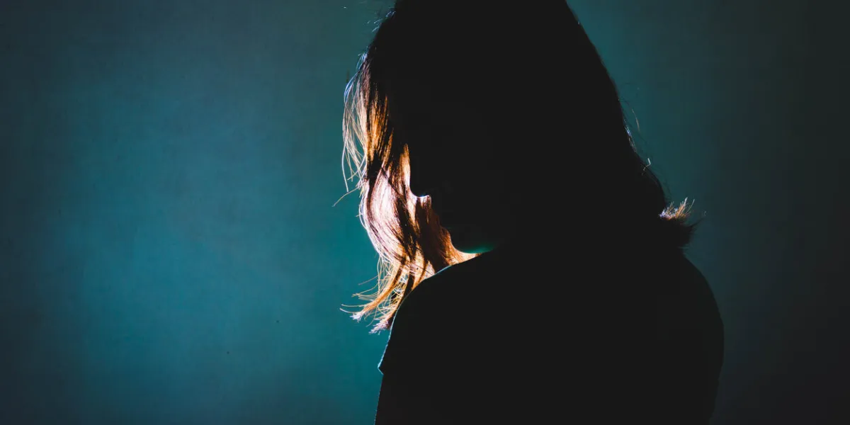 silhouette of depress woman standing in the dark with light shine behind