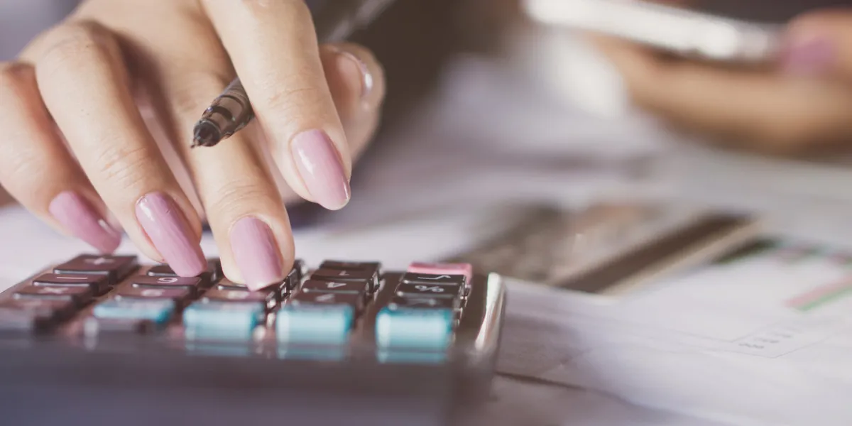 business woman hand counting monthly expenses on calculator with blur background of credit card on table and another hand holding smart phone