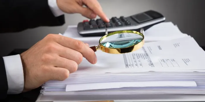close-up of businessperson hands checking invoice with magnifying glass at desk
