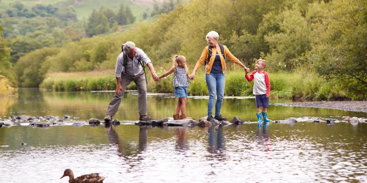grandparents with grandchildren crossing river whilst hiking in uk lake district