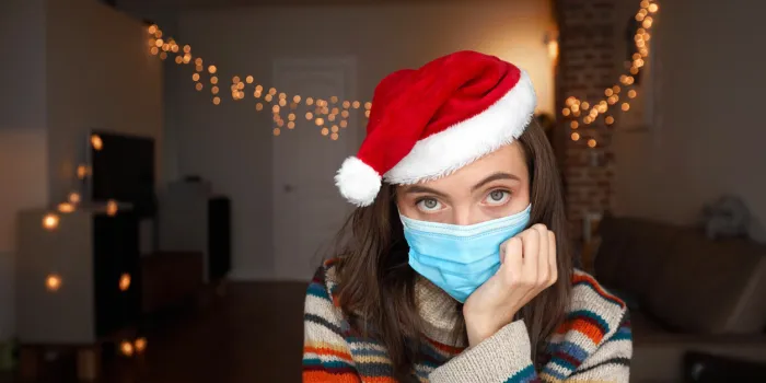 bored lady in coloured pullover and red christmas hat sits in dark room with lights and holds head on hand at home closeup