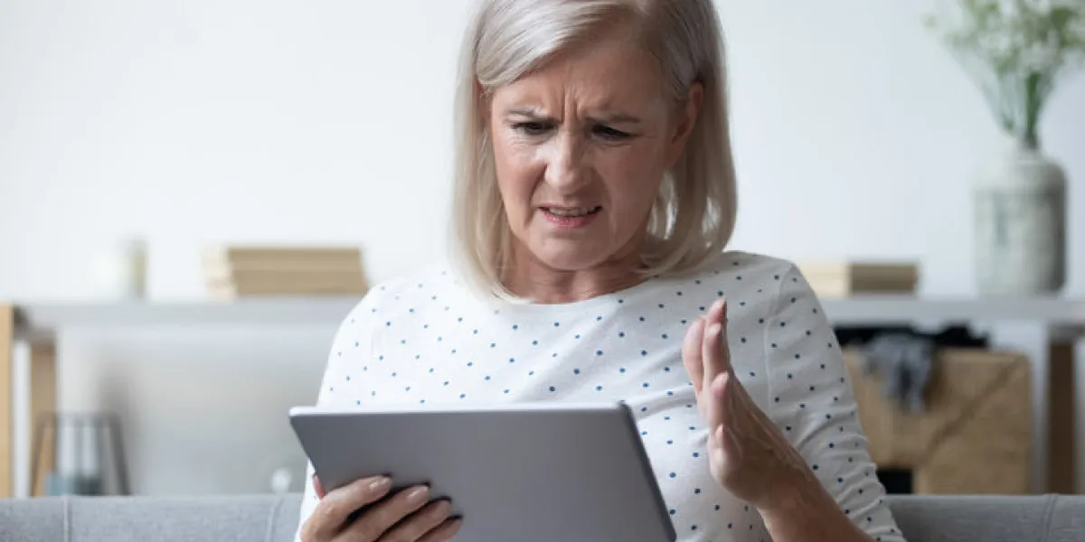 annoyed mature woman having problem with broken or discharged computer tablet, angry older female irritated by spam message or bad news, looking at electronic device screen close up