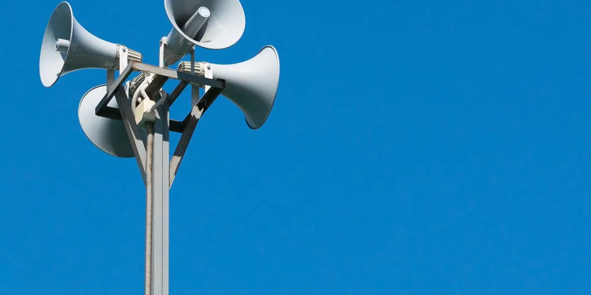 a tall column with four gray loudspeakers in a circle against a clean blue sky hazard warning system the possibility of placing your test or image
