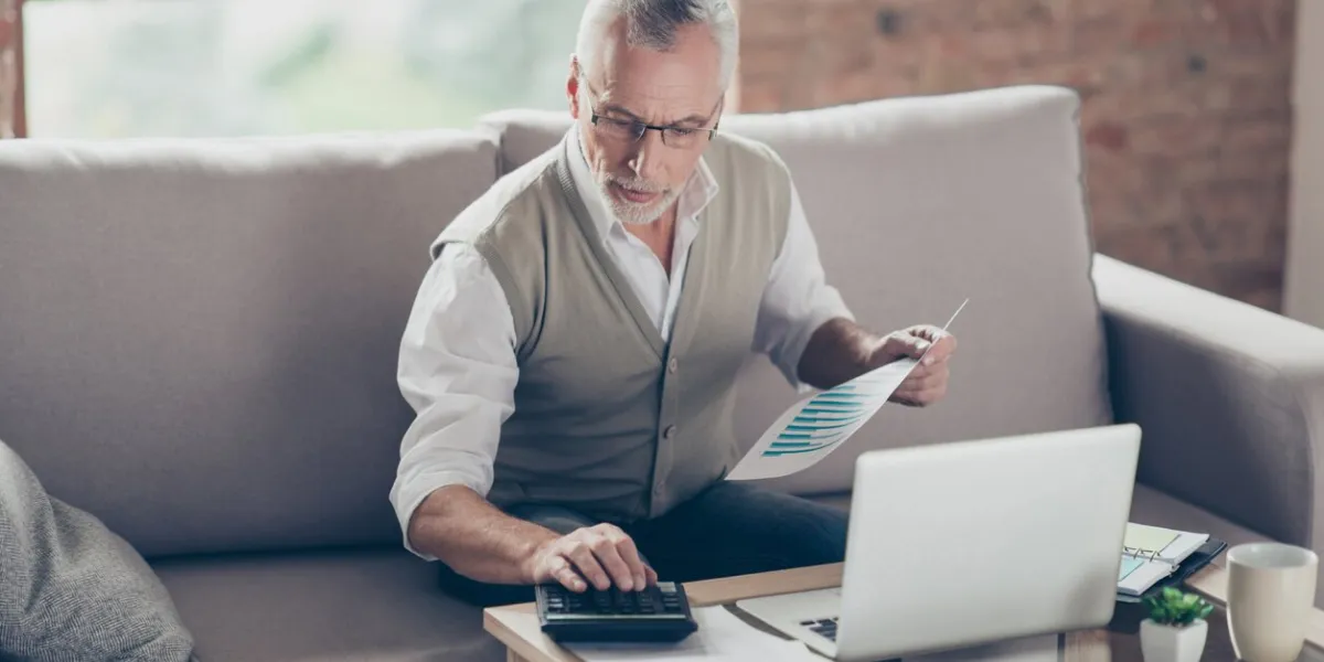 old confident clever concentrated bearded grandpa is checking his calculations sitting in front of monitor at office
