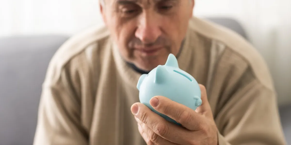 senior caucasian man holding piggy bank with glasses depressed and worry for distress, crying angry and afraid sad expression