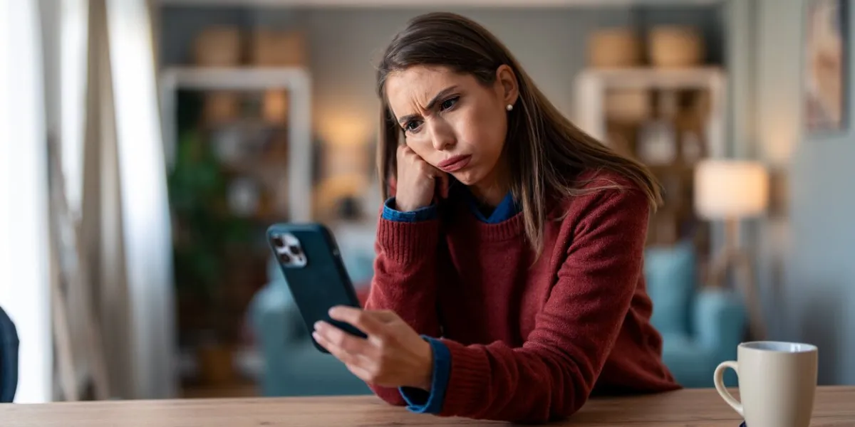 worried disappointed woman looking at mobile phone while sitting at home