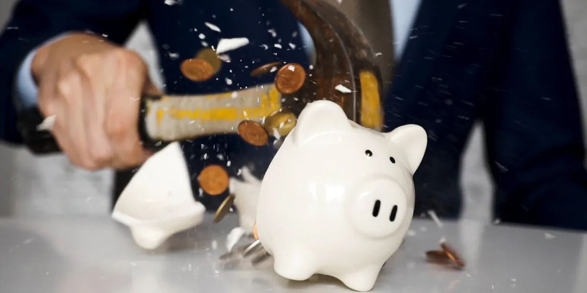 close-up of businessman using a hammer to smash plenty of coins inside piggybank into pieces as he needs emergency money - using money in financial crisis concept
