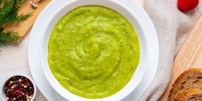 large white bowl with vegetable green cream soup of broccoli, zucchini, green peas on white background, top view