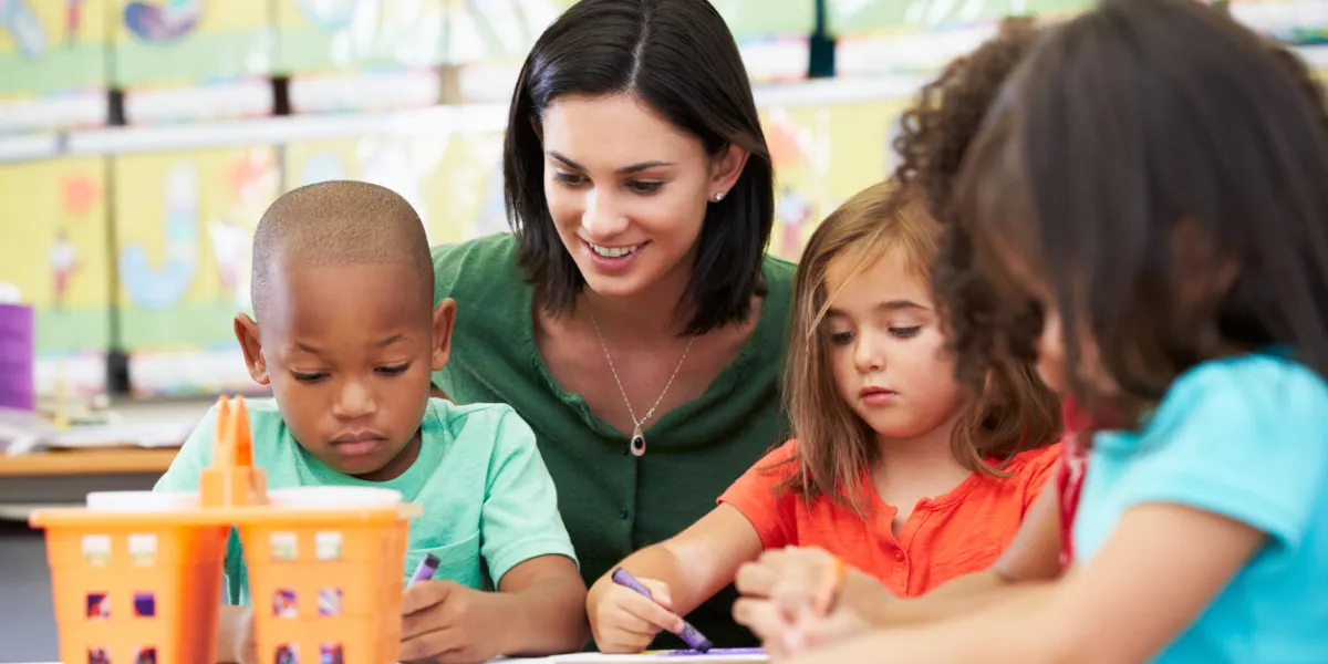 group of elementary age children in art class with teacher sitting down at table drawing