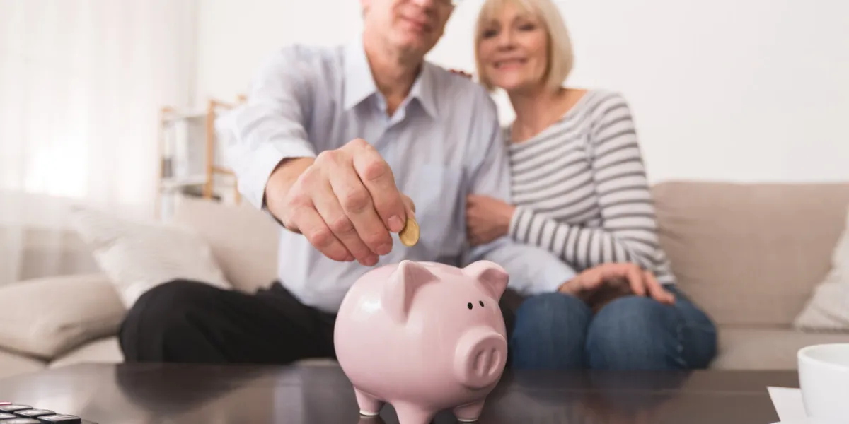 senior couple putting coin in piggybank, saving money at home