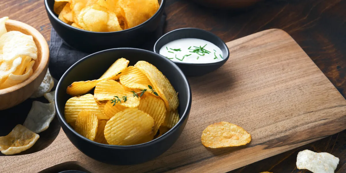 potato corrugatedchips fast food crispy potato chips ceramic black bowl with sour cream sauce and onions in wooden stand on old kitchen table wooden background american tradition hot bbq top view