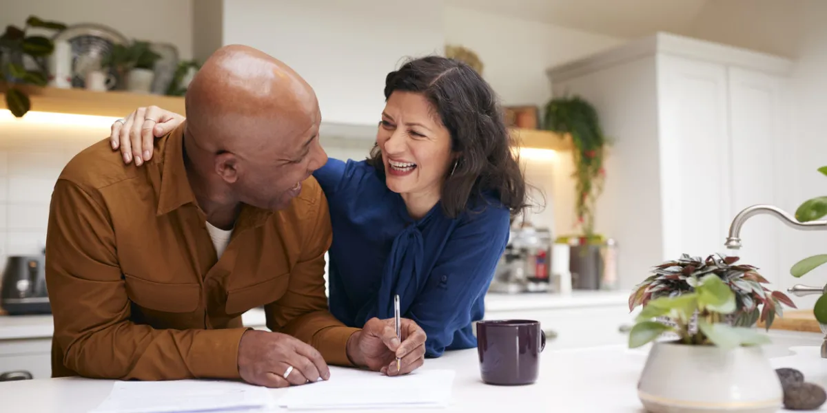 mature couple reviewing and signing domestic finances and investment paperwork in kitchen at home