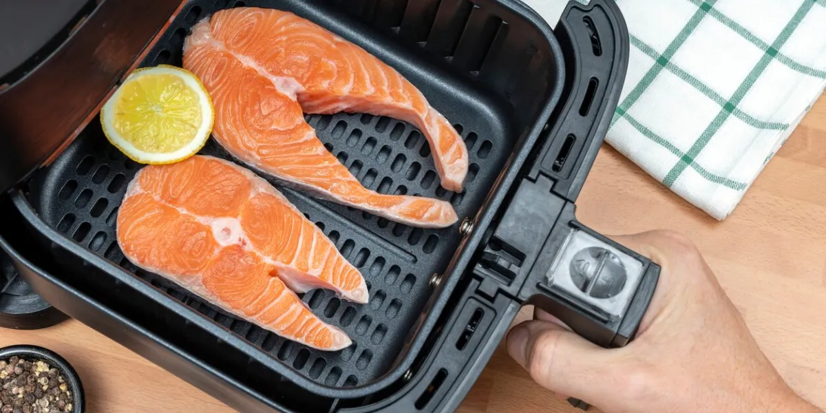 hand holding air fryer basket with two slices of raw salmon ready to cook in the kitchen top view