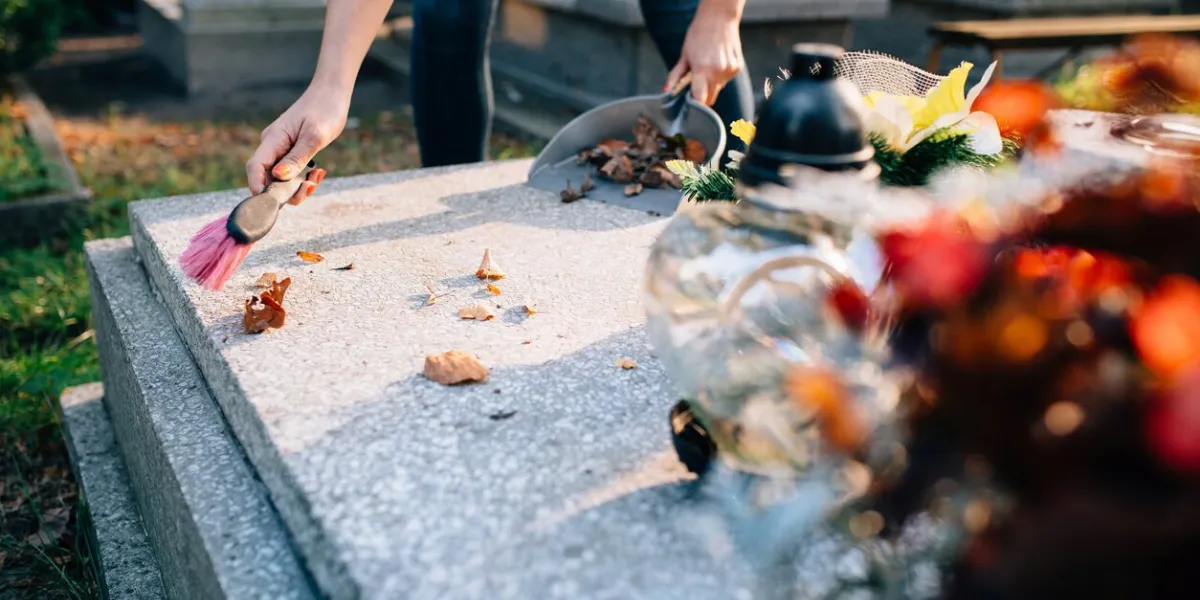 a woman cleans the grave sweeps leaves from the tombstone preparations for all saints day on november