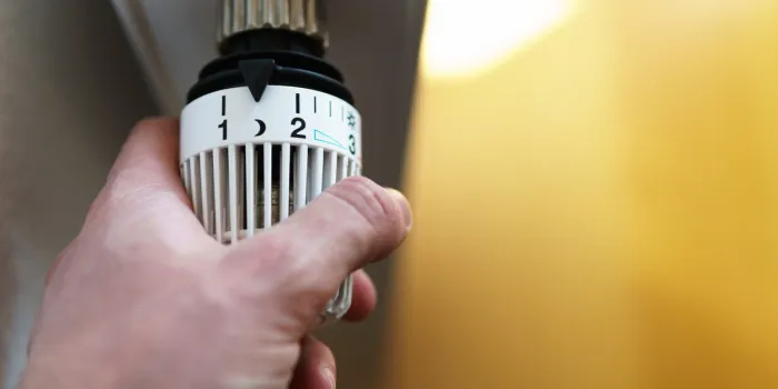 hand of man adjusting radiator thermostat valve down to moon (night) icon, symbol for saving money at heating costs or low temperature setting, closeup, horizontal format, copy space