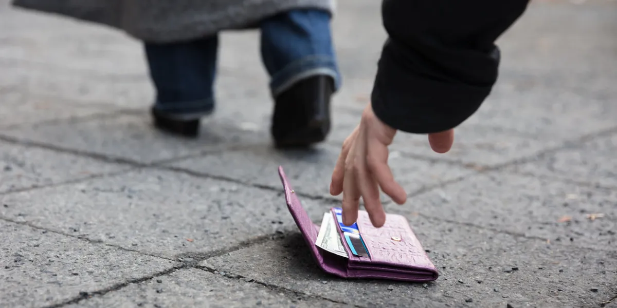 close of a man picking up a lost purse on street