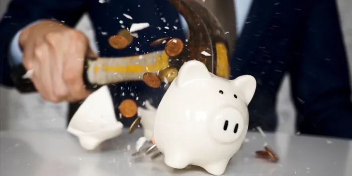close-up of businessman using a hammer to smash plenty of coins inside piggybank into pieces as he needs emergency money - using money in financial crisis concept